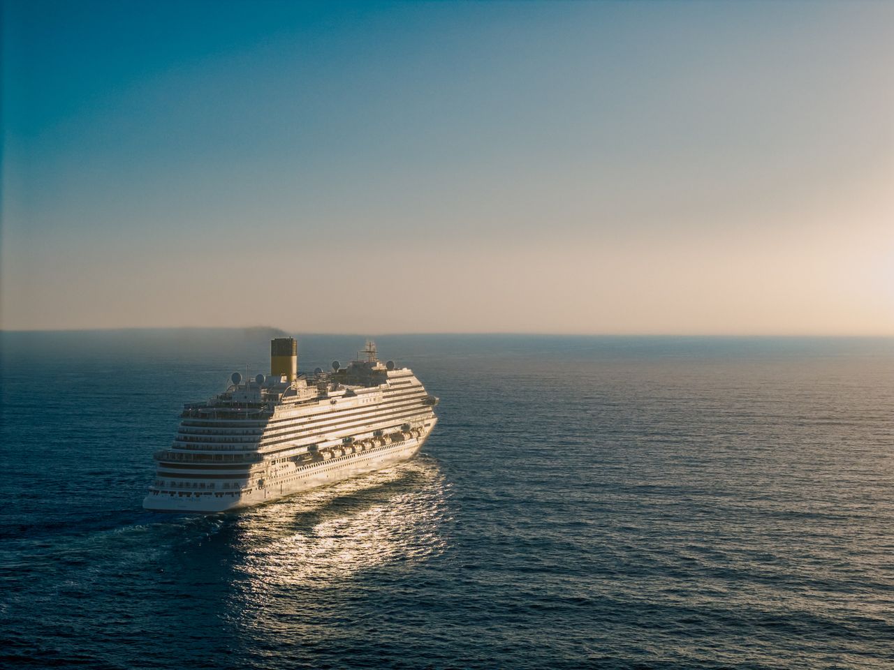A cruise ship gracefully sails across the ocean at sunset, creating a tranquil scene.