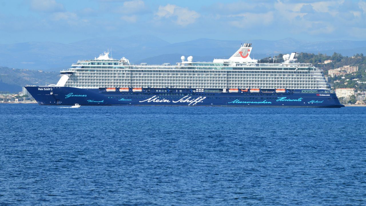 A luxury cruise ship named Mein Schiff sails across the ocean under a clear blue sky.